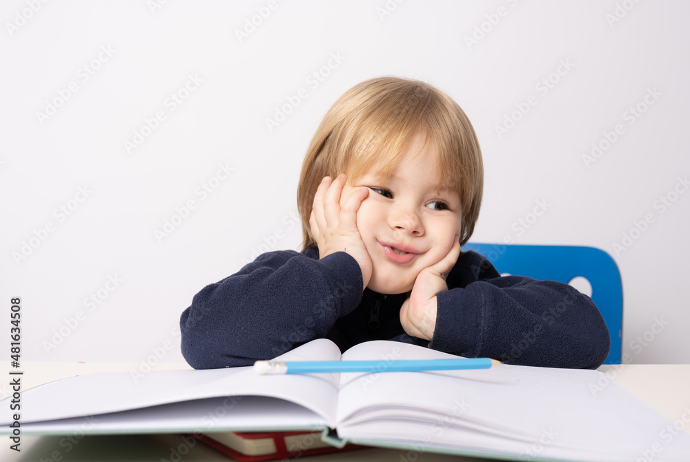 Little boy sitting at the table reading a book isolated over white background. Little boy sitting at the table reading a book isolated over white background.