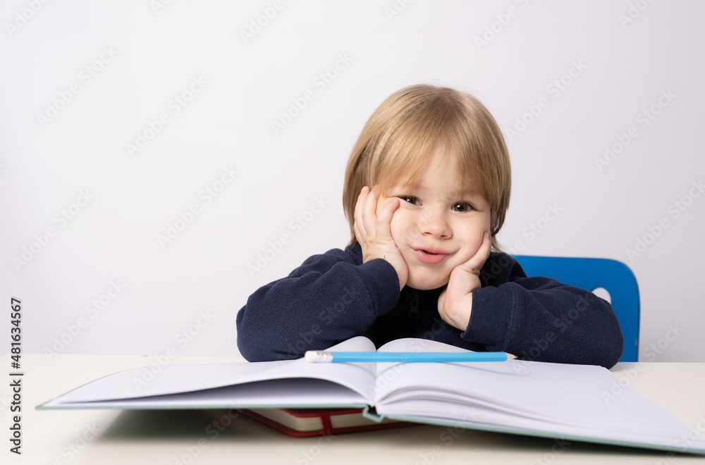 Little boy sitting at the table reading a book isolated over white background. Little boy sitting at the table reading a book isolated over white background.