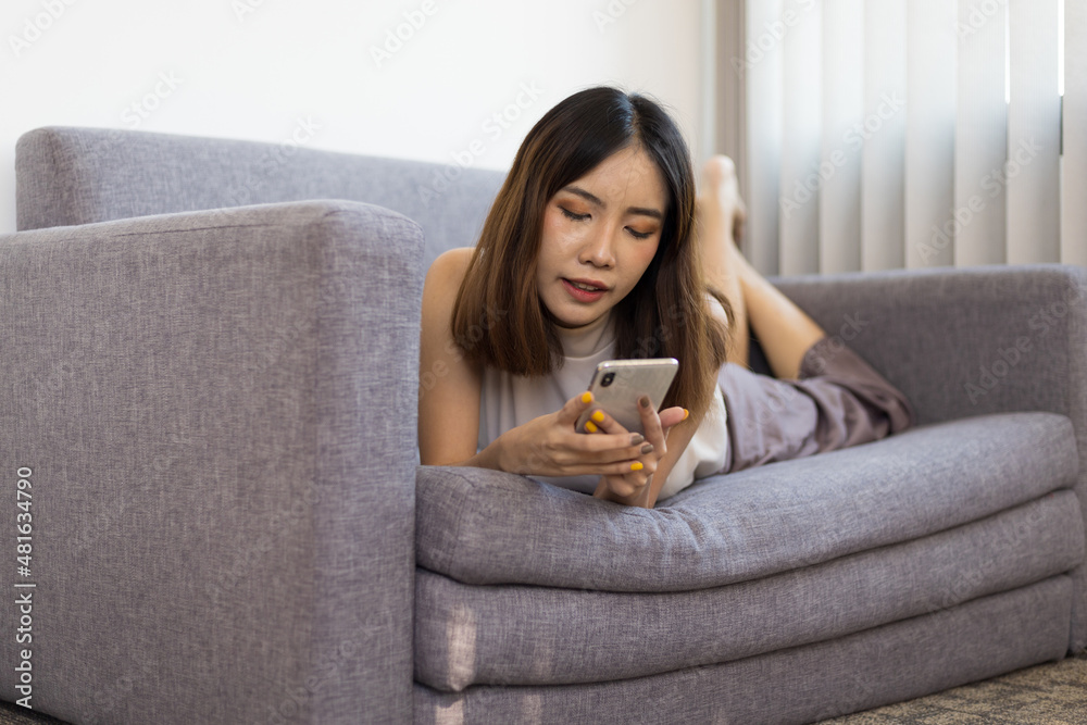 Lifestyle home life Asian woman lying on the sofa in the living room playing mobile phone on the sofa. Lifestyle home life Asian woman lying on the sofa in the living room playing mobile phone on the sofa.