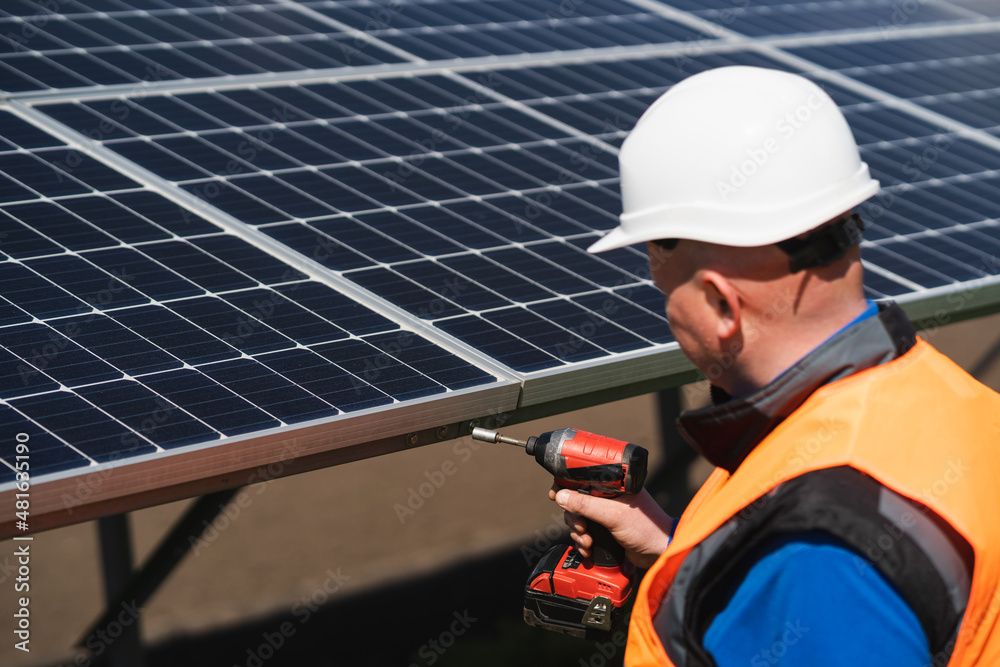 Male electrical engineer in a hard hat with electric wrench maintains solar panels at power plant Male electrical engineer in a hard hat with electric wrench maintains solar panels at power plant