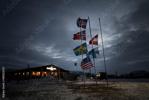 various flags of the Nordic countries are flying on the flagpole in wind against the background of the night sky in the clouds. Dramatic landscape photo