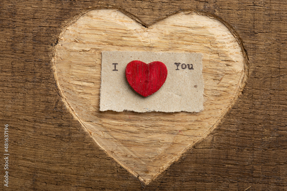 Fototapeta premium I love you - tiny typed text note close up. Valentines Day greetings concept. Carved heart shape on wood as background for Valentines greeting card.