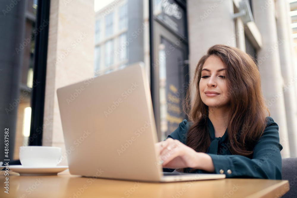 Uses a laptop and writes a message to the client. A woman in a formal dress works in a cafe Uses a laptop and writes a message to the client. A woman in a formal dress works in a cafe