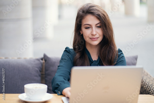 Uses a laptop and writes a message to the client. A woman in a formal dress works in a cafe