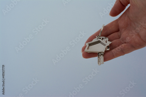 Real estate agent holding key with house shaped keychain on blue background. Mortgage concept. Moving home or renting property. Copy space