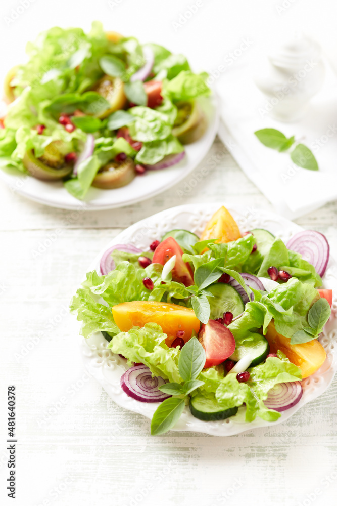 Salad with red and yellow Tomatoes and Pomegranate Seeds on bright wooden Background. Close up. Salad with red and yellow Tomatoes and Pomegranate Seeds on bright wooden Background. Close up.