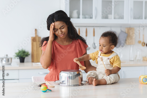 Black mother suffering headache while her infant baby making noise in kitchen