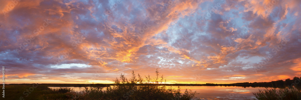 Fototapeta premium textured panorama of a colorful sunset over a lake with textured clouds and reflection in the water