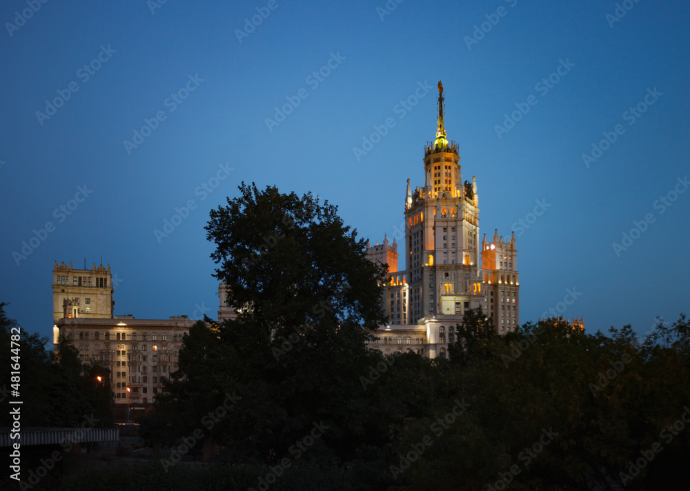 The High-rise building on the Kotelnicheskaya Embankment of Moskva river called Stalin skyscraper. With city lights. Evening blue sky.