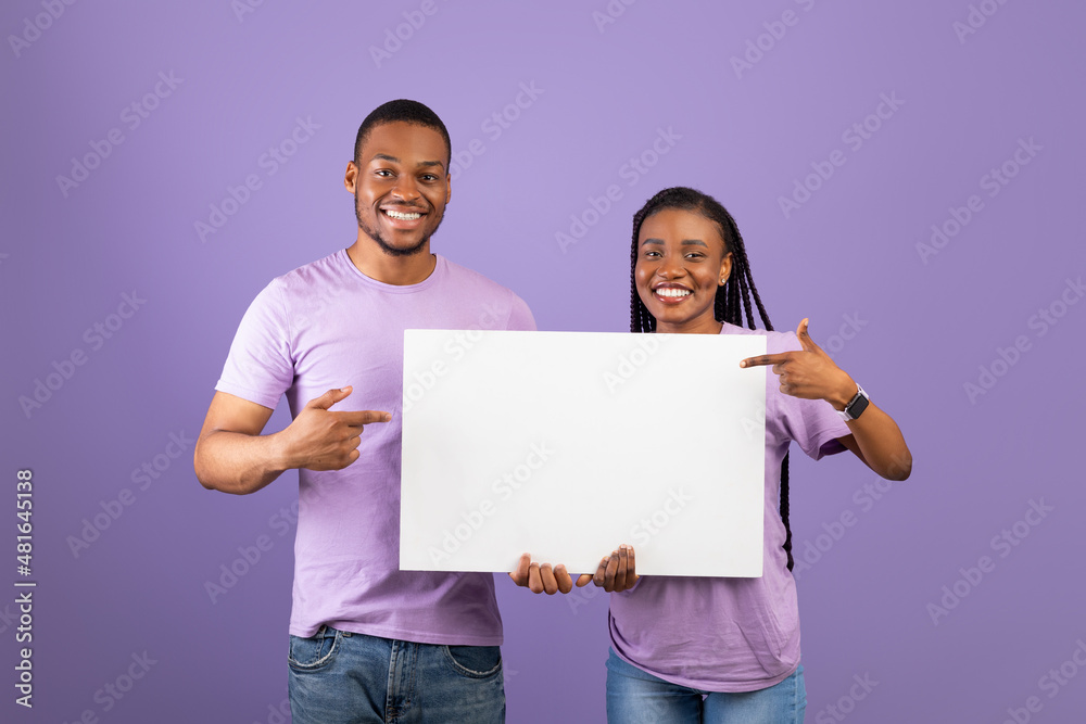 Black couple holding and pointing at blank white advertising placard Black couple holding and pointing at blank white advertising placard