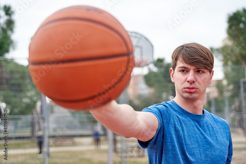 Handsome sportsman standing on basketball court background with basketball in hand