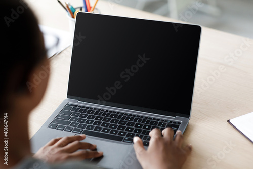 Teen afro american schoolgirl in glasses typing on laptop