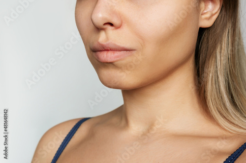 A lower part of a young caucasian blonde woman's face with clear highlighted cheekbones isolated on a gray backgroud. Plastic surgery buccal fat removal. Result of cosmetic surgery