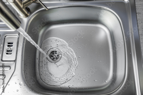 Wasser fliesst aus einem Wasserhan in ein Spülbecken