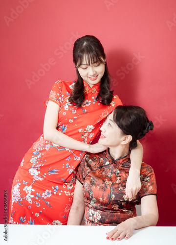 Mature asian mother hugging with her asian daughter on red background(Both wearing traditional cheongsam qipao).