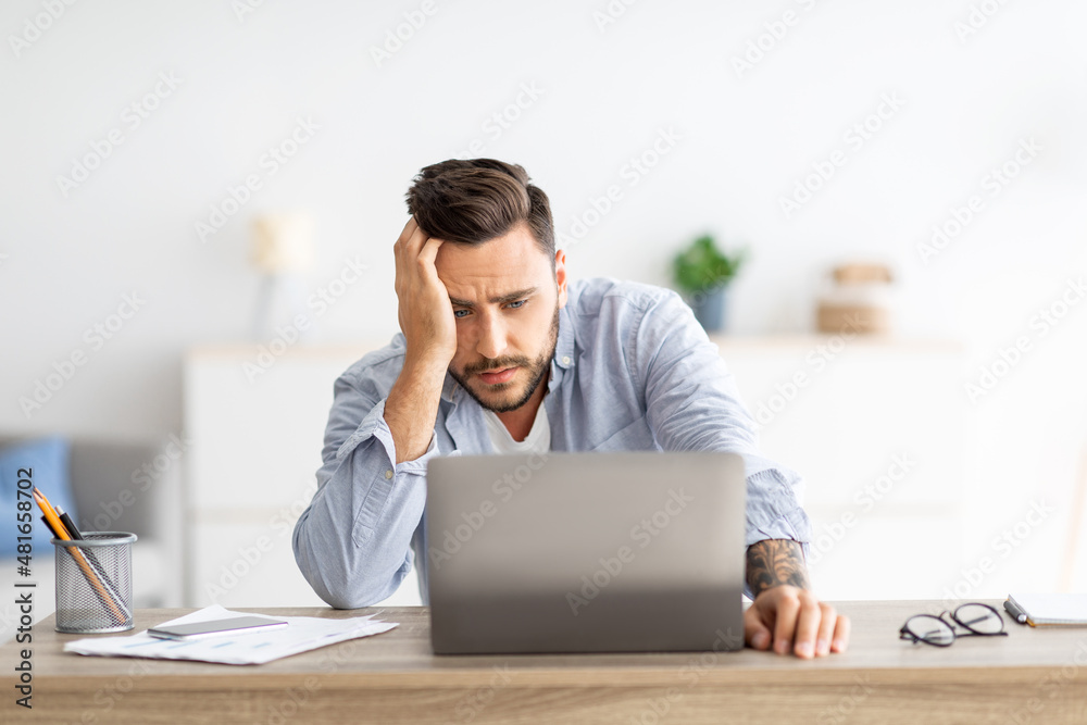 Freelance stress. Male freelancer tired after work on laptop at home, having problems with project, sitting at workplace Freelance stress. Male freelancer tired after work on laptop at home, having problems with project, sitting at workplace