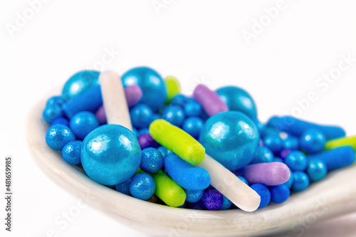 Blue, green, purple sugar sprinkles in a small white spoon.