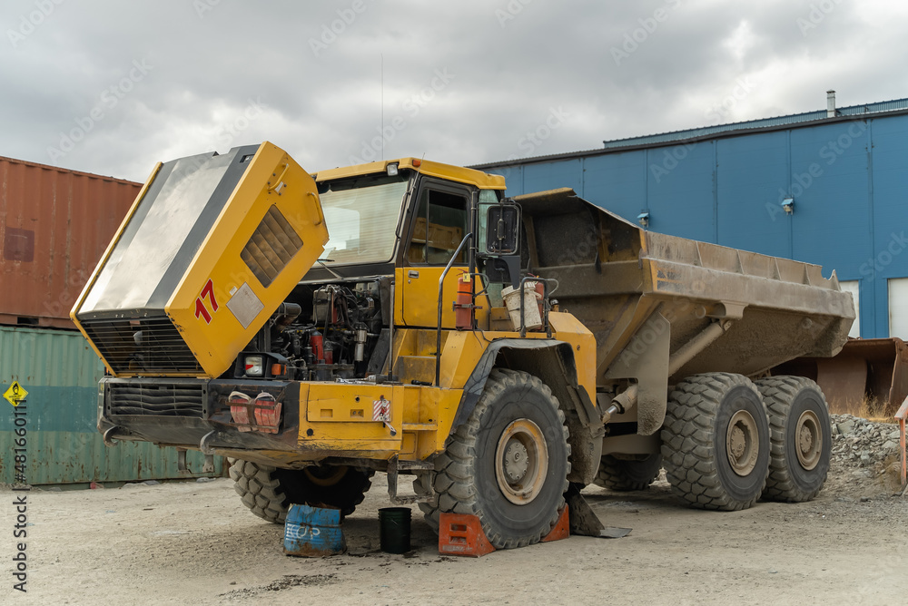 An articulated dump truck waiting to be repaired stands near the containers at the gold mine site. An articulated dump truck waiting to be repaired stands near the containers at the gold mine site.
