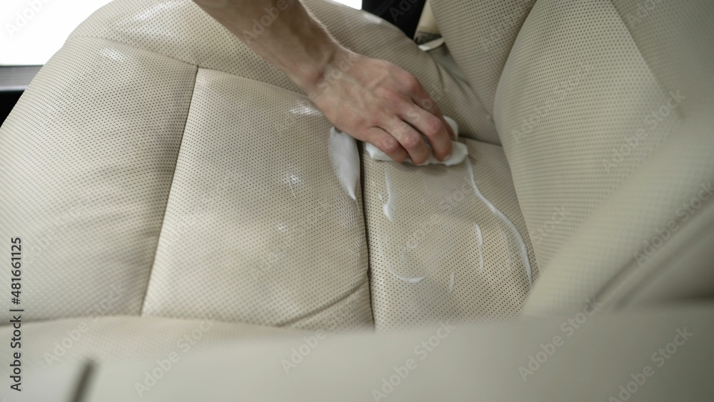 Obraz premium Dirty car interior. cleaning the white leather seat of the machine with a special cleaner. White foam from the cylinder. wiping with a cloth. Dry cleaning of white leather interior.