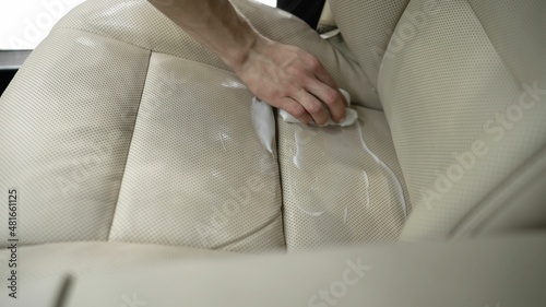 Dirty car interior. cleaning the white leather seat of the machine with a special cleaner. White foam from the cylinder. wiping with a cloth. Dry cleaning of white leather interior.