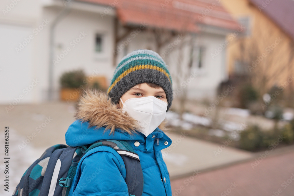 Kid boy wearing ffp medical mask on the way to school. Child backpack satchel. Schoolkid on cold autumn or winter day with warm clothes. Lockdown and quarantine time during corona pandemic disease Kid boy wearing ffp medical mask on the way to school. Child backpack satchel. Schoolkid on cold autumn or winter day with warm clothes. Lockdown and quarantine time during corona pandemic disease