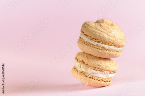 Two beige macaroons in a stack close-up on a pale pink background with copy space