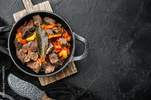 Goulash, beef stew, in cast iron frying pan, on black stone background, top view flat lay, with copy space for text