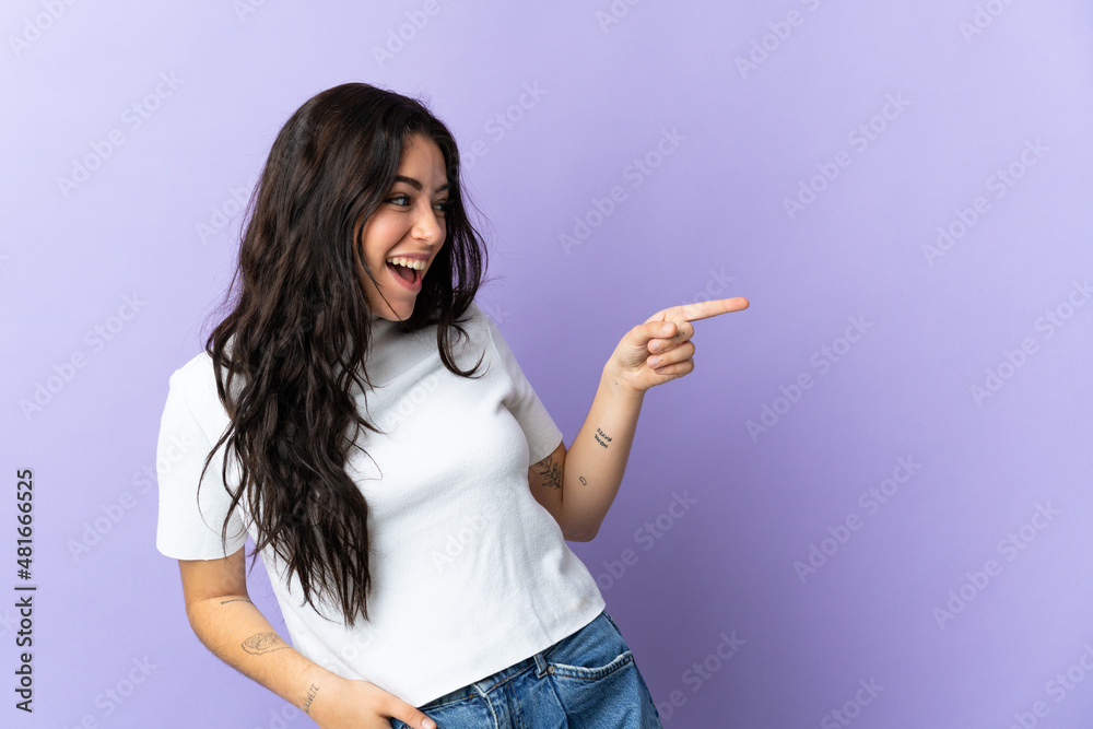 Young caucasian woman isolated on purple background pointing finger to the side and presenting a product Young caucasian woman isolated on purple background pointing finger to the side and presenting a product