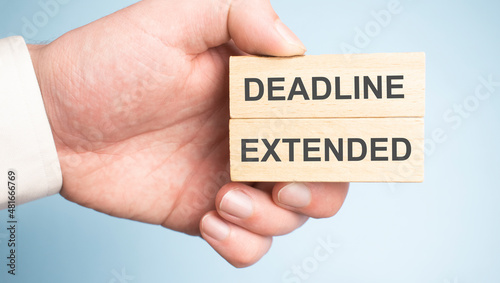 Male hands holding two wooden pegs with DEADLINE EXTENDED sign