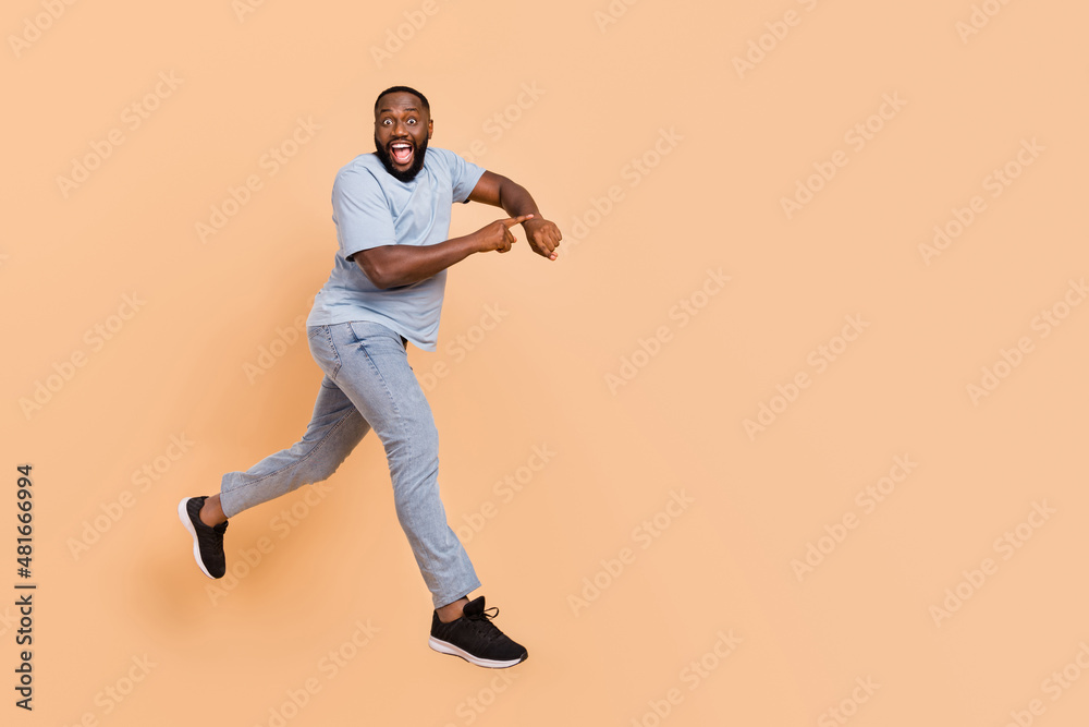 Full length body size view of attractive cheerful guy jumping showing time running isolated over beige pastel color background Full length body size view of attractive cheerful guy jumping showing time running isolated over beige pastel color background
