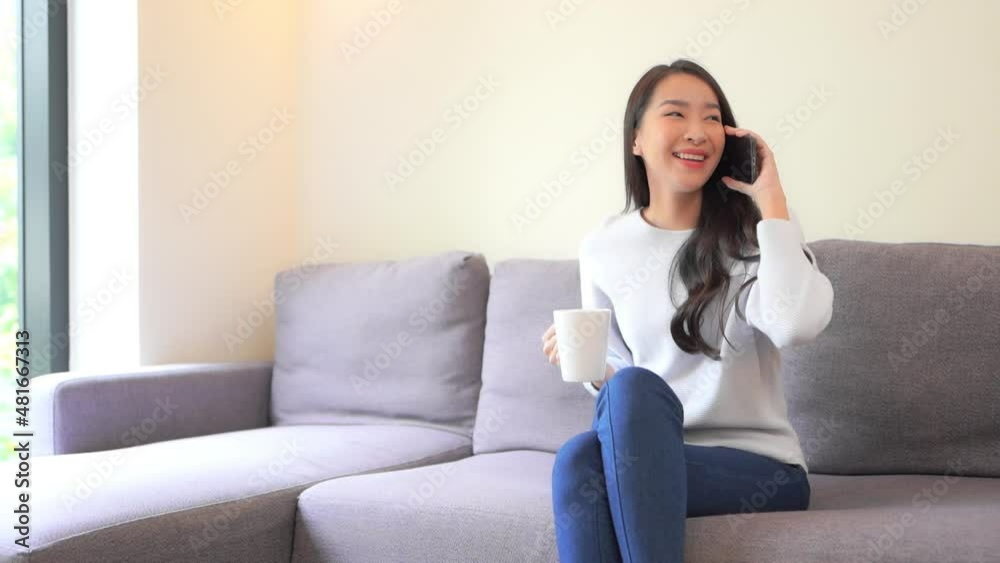 A young woman in jeans and a sweater holds a cup of coffee in one hand and talks on a smartphone held in the other. Title space