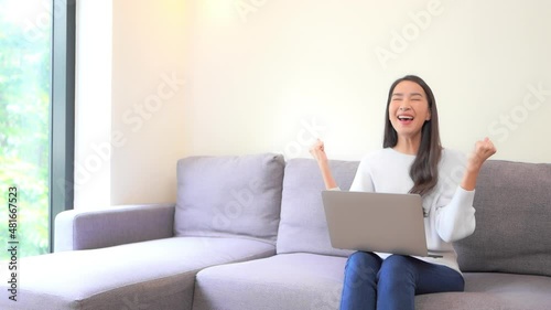 A young woman working on her laptop reacts in triumph as she completes her task. Title space photo