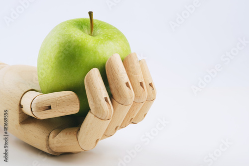 Leinwand Poster Wooden hand holding a granny smith apple on a white background.