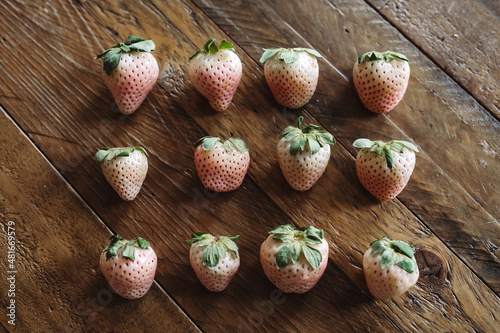 Fresh Fruit Flat Lay. 3 Rows of Pineberries on Wooden Table. White Strawberries. Seasonal Fruit Still Life. Pink and White Berries on Dark Background.