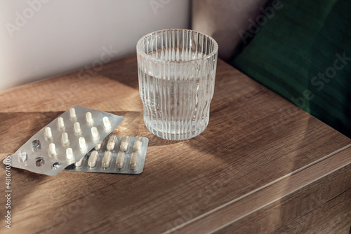 Pills capsules medicine and glass of water on wooden background
