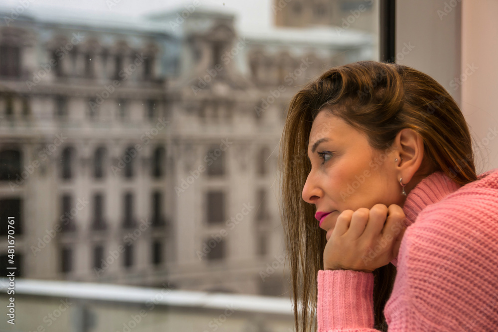 Woman Next To A Window And Looking Away. She Is Contemplating The Panorama Outside, Looking Outside Through A Window