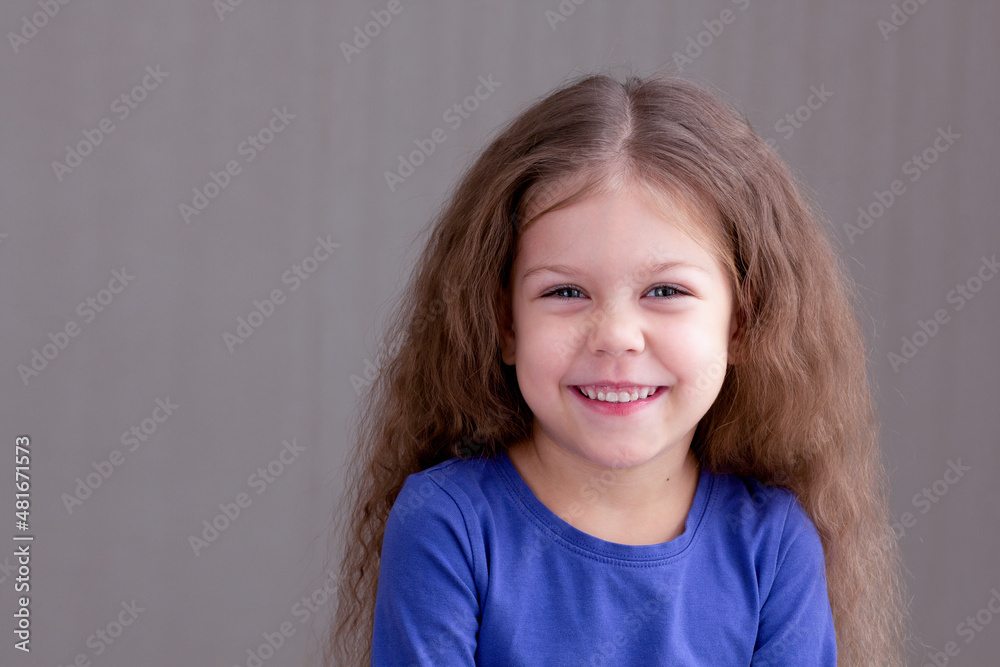 Happy smiling child kid on gray background looking at camera portrait of caucasian little girl of 5 years in blue Happy smiling child kid on gray background looking at camera portrait of caucasian little girl of 5 years in blue
