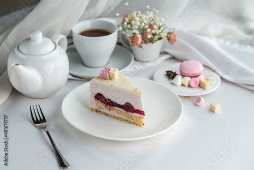Delicious cherry mousse cake slice with the layers and cup of tea on the table