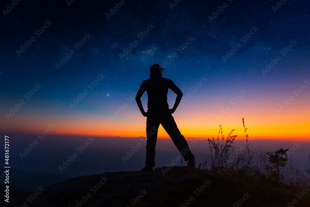 Milky Way. Colorful night sky with stars and silhouette of a standing man on the stone. Blue milky way with man on the mountain. High Rocks. Background with galaxy and silhouette of a man. Universe 