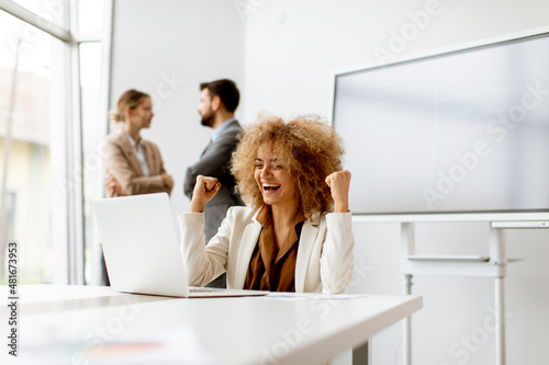 Foto Young joyful businesswoman using laptop in the office with young people works be