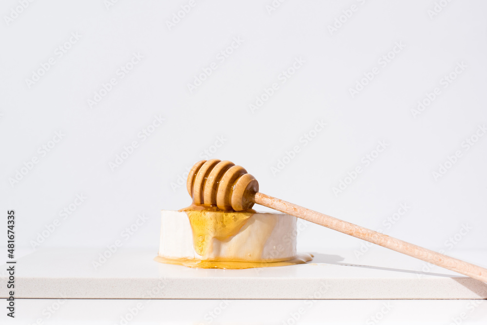 Verter la miel sobre el queso de cabra, con gotero de madera. Aperitivo comida mediterránea sobre fondo claro