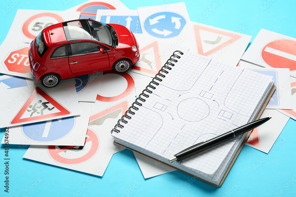 Many different road sign cards, notebook with sketch of roundabout and toy car on light blue background. Driving school Many different road sign cards, notebook with sketch of roundabout and toy car on light blue background. Driving school