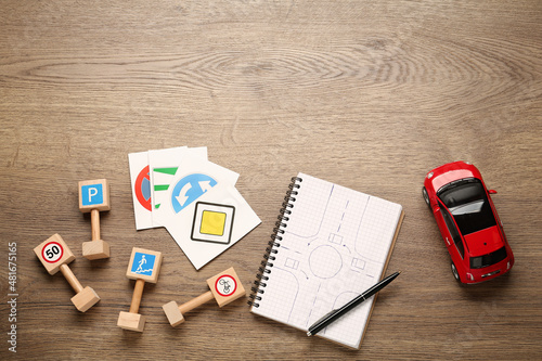 Many different road signs, notebook and toy car on wooden background, flat lay with space for text. Driving school photo