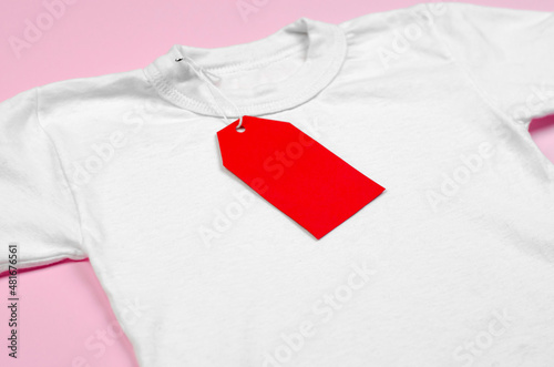 Blank red price tag on white t-shirt. White t-shirt on a pink background with a red blank label.