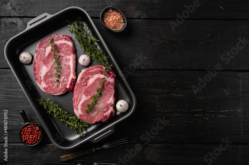 Raw rib eye steak of beef, on black wooden table background, top view flat lay, with copy space for text