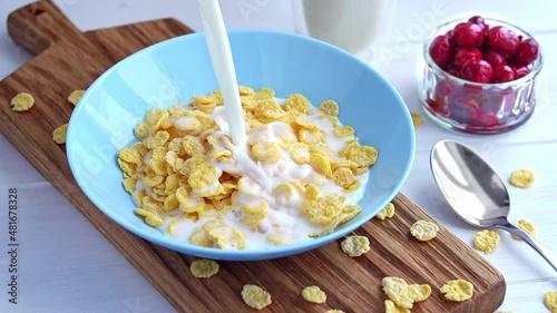 Pouring milk into blue bowl full of crunchy cornflakes cereal in slow motion. Healthy breakfast concept