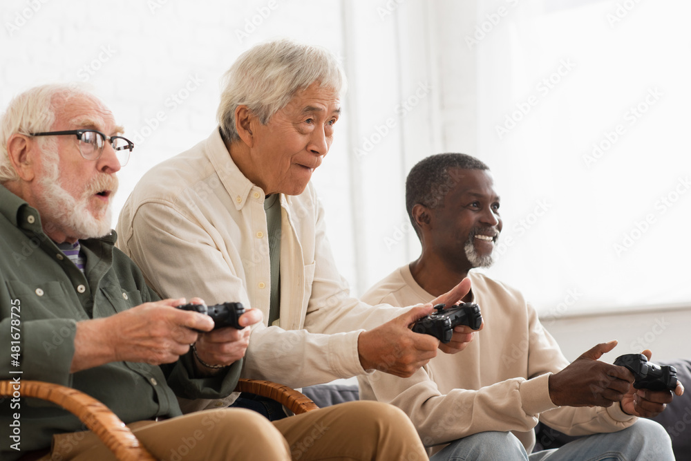 Obraz premium KYIV, UKRAINE - OCTOBER 12, 2021: Focused multiethnic senior men playing video game at home.