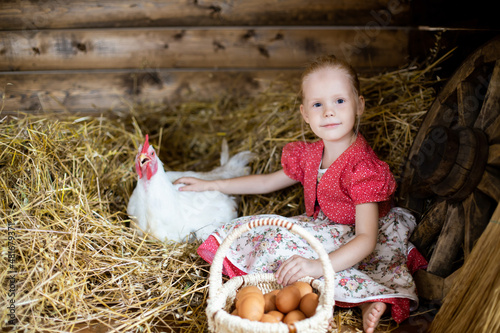 A girl with a chicken, a little girl in the village is sitting in the hay, at her grandmother's in the village, a girl with a pockmarked chicken, children in the village.