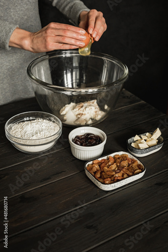 Baking sweet cottage cheese braided bread with raisins and jam. Ingredients on a wooden table. Beating an egg into a big bowl. Lifestyle image.