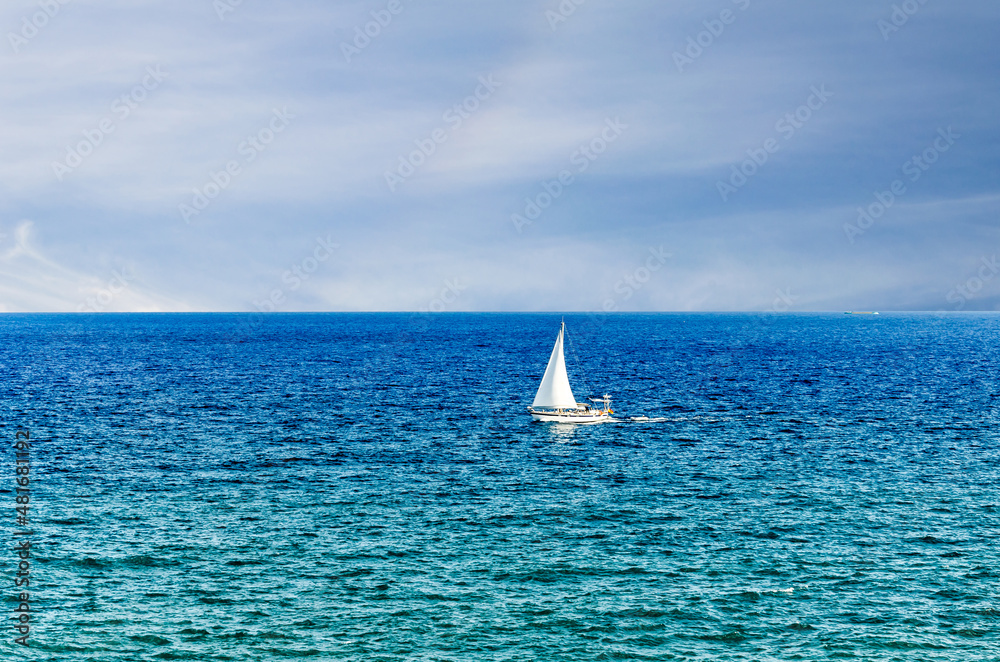 Scene of a small boat with sail in the middle of the blue ocean